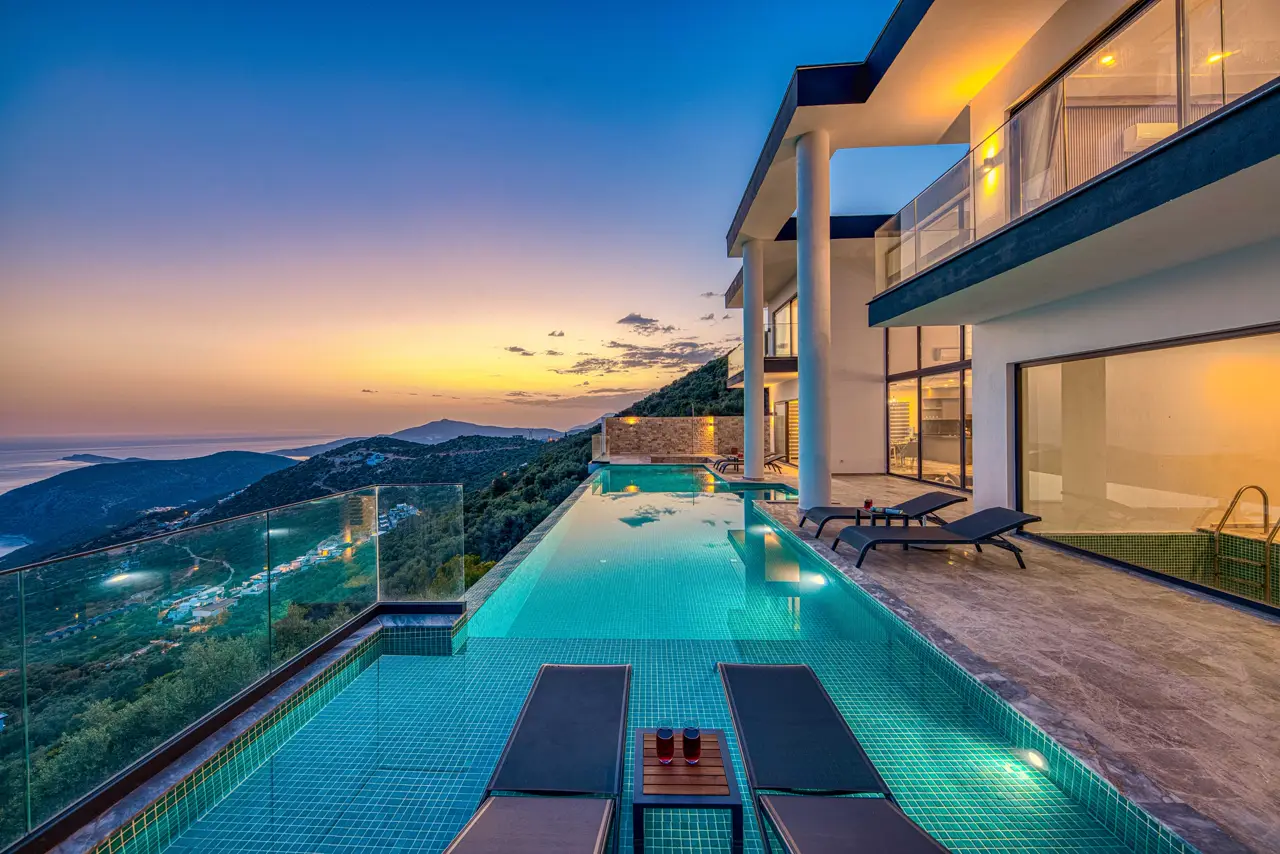 A pool villa at dusk, lights on, terrace open to the hills